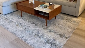 A living room with a grey sofa, a wooden coffee table, and a patterned rug.