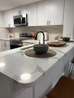 Cozinha moderna com armários brancos, micro-ondas e forno de aço inoxidável.