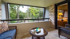 A balcony with wicker furniture, a glass table, and a view of trees.