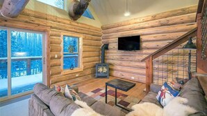 Ein Blockhaus-Interieur mit Kamin, Fernseher und einer Couch.