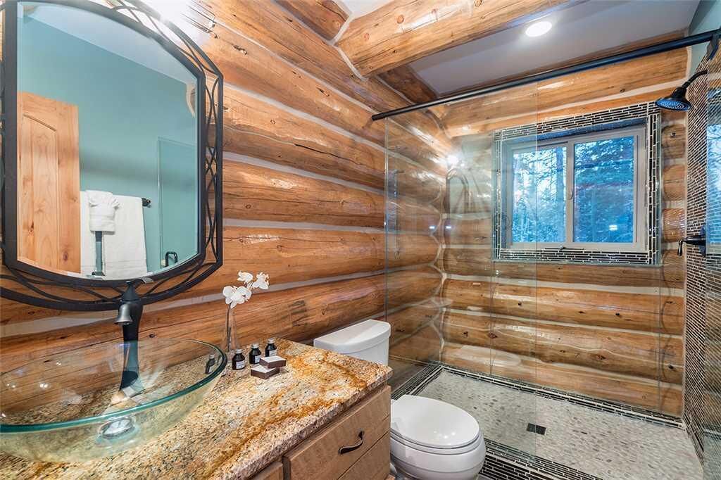 A log cabin bathroom with a glass shower enclosure, a round mirror, and a granite countertop.