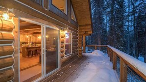 Eine Blockhütte mit Glastür und Eingang zu einem Küchenbereich, umgeben von verschneitem Gelände und einer Holzdiele.