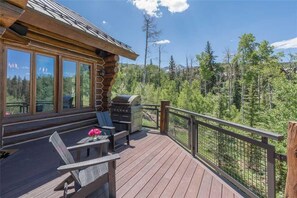 A wooden deck with a grill and seating area, overlooking a forested landscape. - Slopeside Lodge (Telluride)