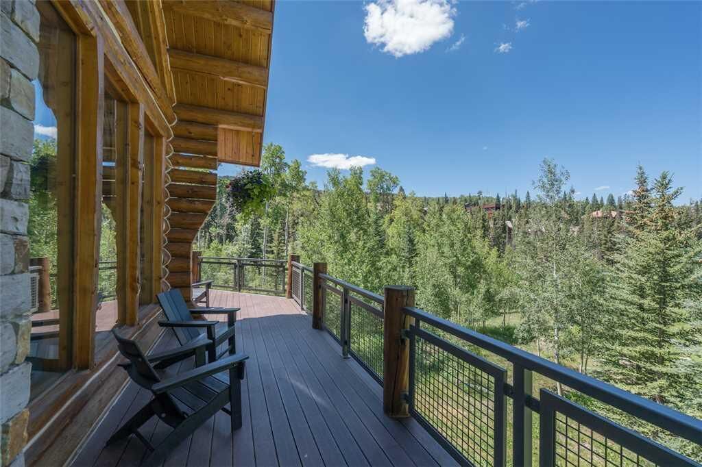 A wooden deck with chairs, a stone wall, and a view of a forested mountain.