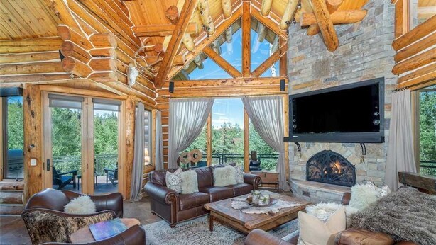 L’intérieur d’une cabane en rondins, avec une cheminée en pierre, des meubles en cuir et de grandes fenêtres donnant sur le paysage extérieur.