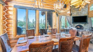 Une cabane en bois dotée d’un coin repas, de grandes fenêtres et d’une cheminée en pierre.