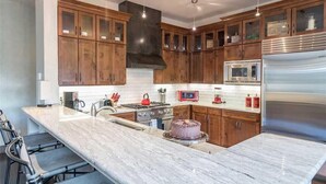 A modern kitchen with wooden cabinets, a stainless steel refrigerator, a microwave, and a marble island. - Cassidy Ridge C301- Fawns Leap (Telluride)