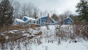 A blue house with a sloped roof, surrounded by snow-covered ground and trees. - Mid_modern 4 BR (Stowe)