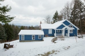 Una casa azul de dos pisos con techo nevado y un pequeño garaje adosado.