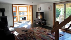 A modern living room with a fireplace, a television, and a large window. - Mid_modern 4 BR (Stowe)