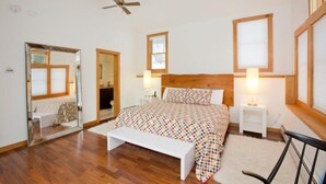 A bedroom with a wooden headboard, a large bed with patterned bedding, two bedside tables with lamps, a bench, and a ceiling fan. - Mid_modern 4 BR (Stowe)