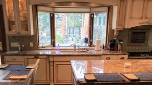 A kitchen with wooden cabinets, a large window, and a central island with stools. - Sunny Mountain Chalet with Views & Chief's Kitchen, River, Hot Tub, Bar, AC, Pet (Estes Park)