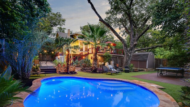 A swimming pool surrounded by a landscaped garden, a wooden deck, and a house with a red railing and outdoor lighting. - Austin Oasis Near UT and Downtown (Austin)