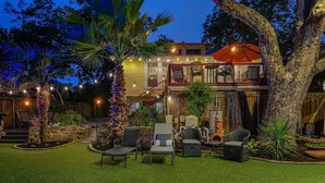 A two-story house with a balcony, outdoor seating area with chairs and a table, and a large tree in the foreground. - Austin Oasis Near UT and Downtown (Austin)