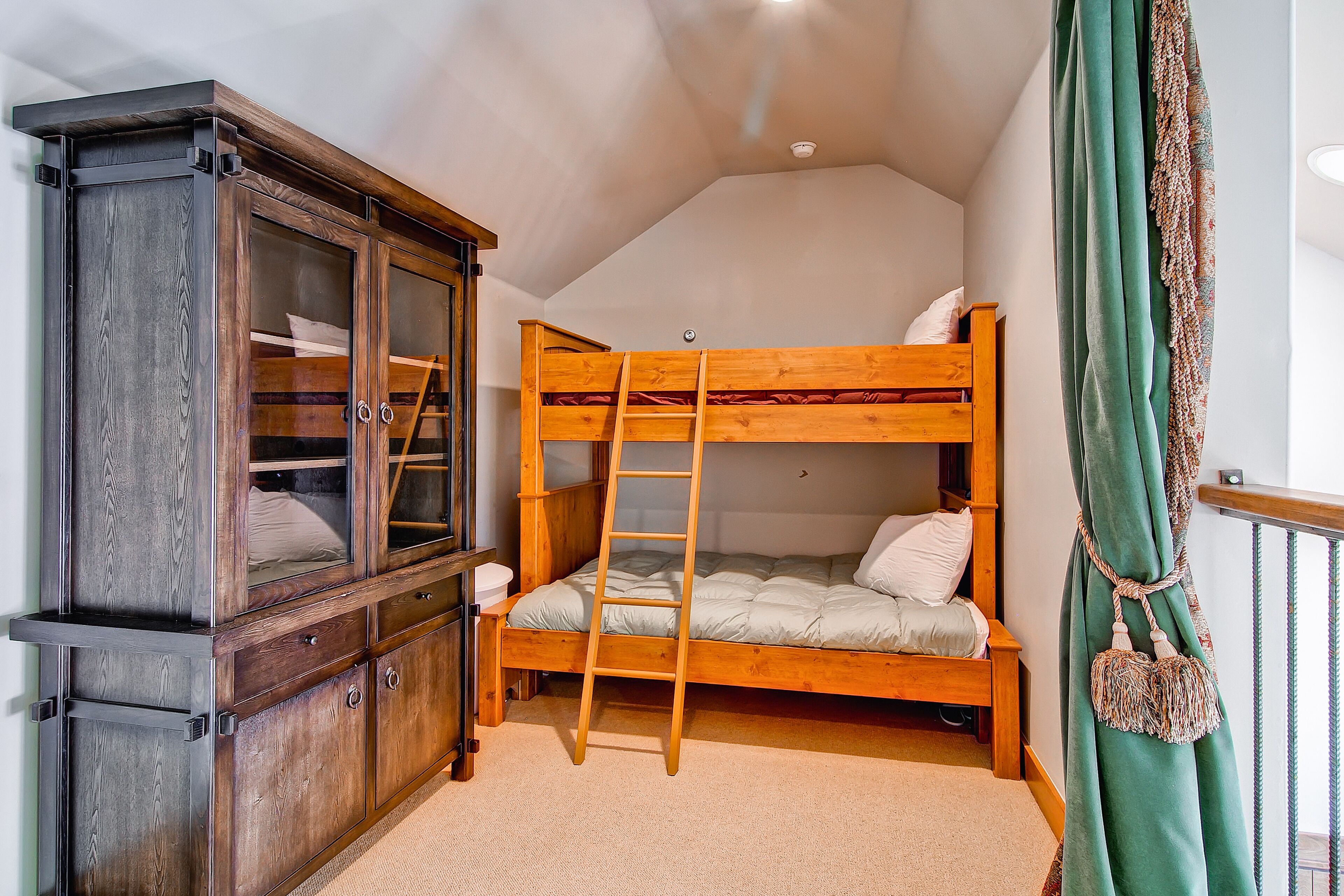 A bunk bed with a ladder, a wooden cabinet with glass doors, and a green curtain.