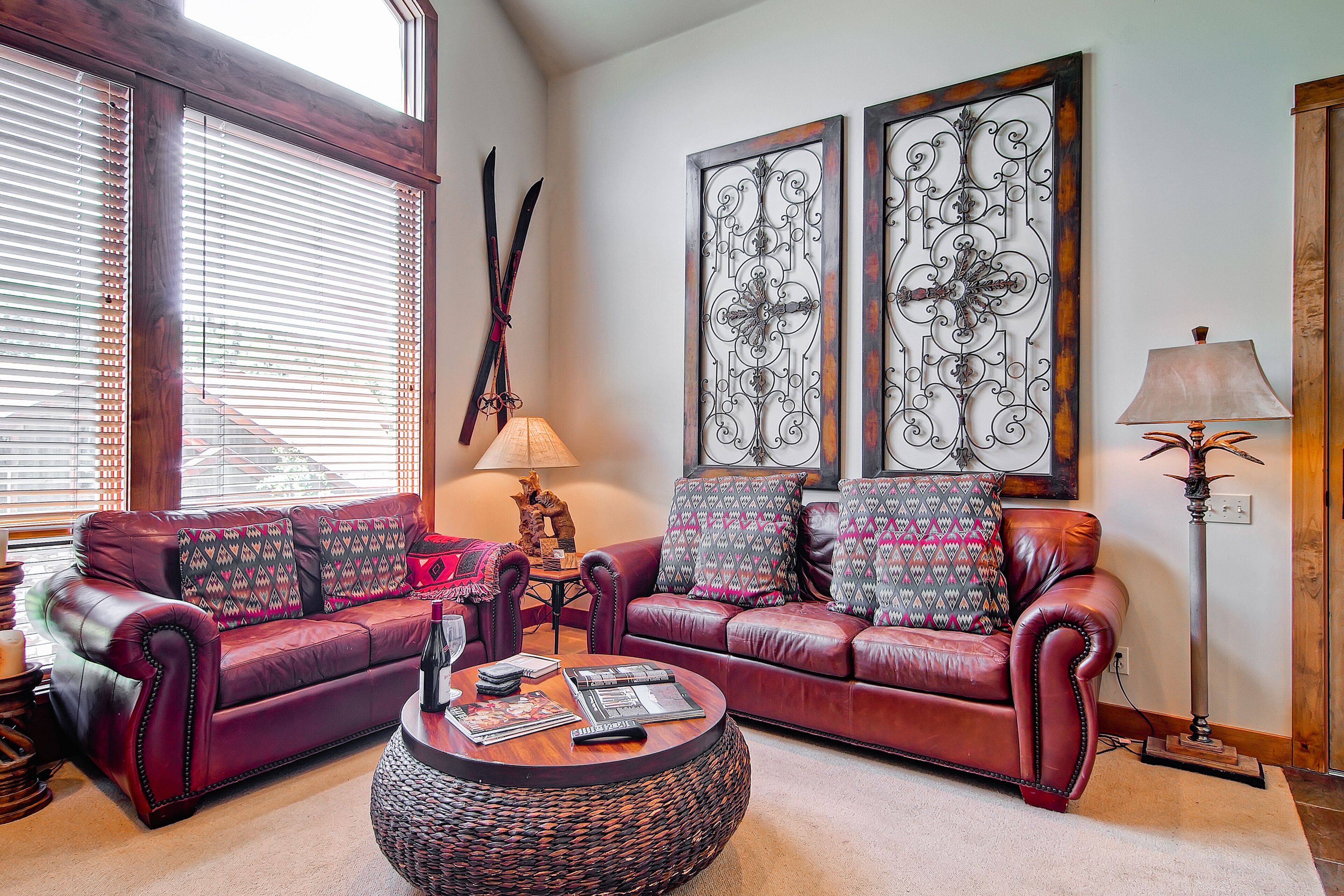 A living room with a red leather sofa, patterned cushions, a round coffee table, and two wall-mounted decorative panels.