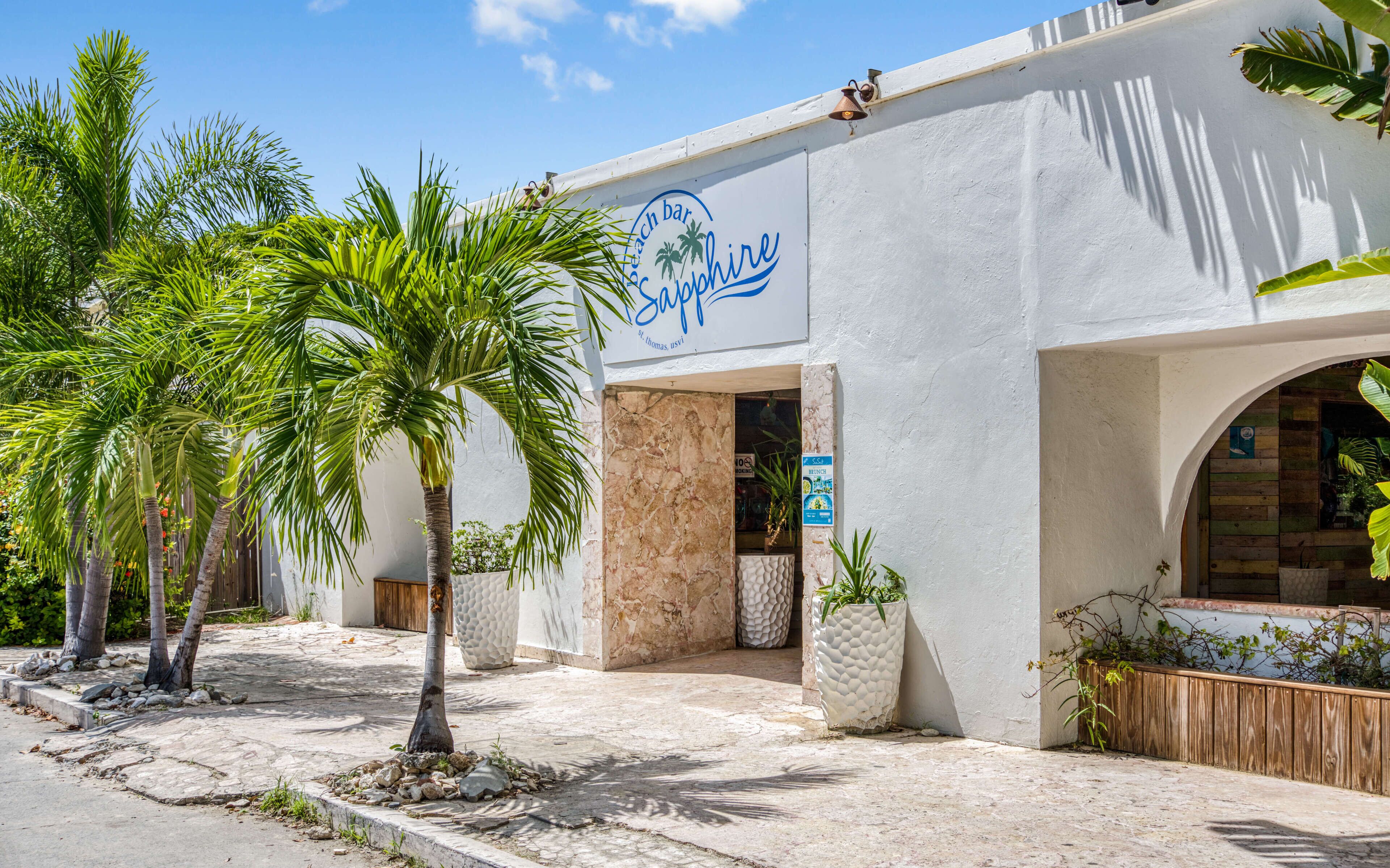 A beach bar named 'Sapphire' with a white facade, palm trees, and a stone pathway.