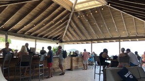 An outdoor covered area with wooden beams, bar counters, and seating. - Sapphire Beach, Crystal Cove Condo. Prime Location. Steps to Turquoise Water! (St. Thomas)
