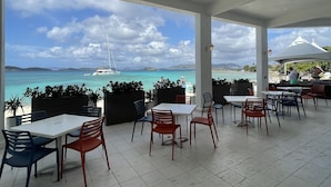 An outdoor seating area with tables and chairs, overlooking a beach and the sea. - Sapphire Beach, Crystal Cove Condo. Prime Location. Steps to Turquoise Water! (St. Thomas)