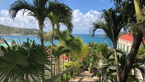 A pathway leading to a building with a red roof, surrounded by lush greenery and overlooking a coastal area with boats. - Sapphire Beach, Crystal Cove Condo. Prime Location. Steps to Turquoise Water! (St. Thomas)