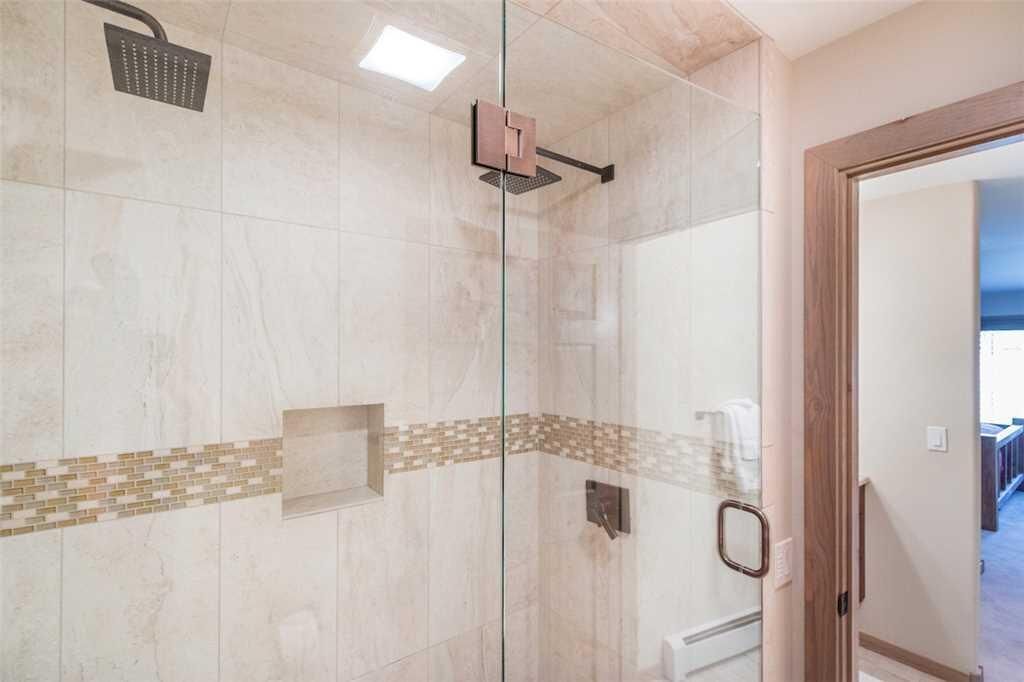 A glass-enclosed shower with a handheld showerhead and a wall-mounted control panel.