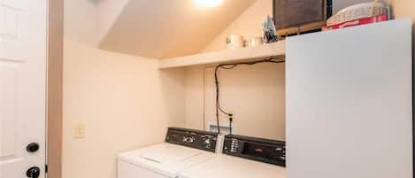 A laundry room with a washer and dryer, a shelf with items, and a door.
