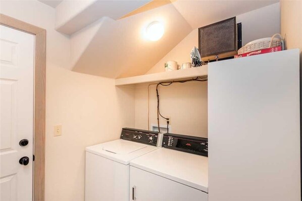 A laundry room with a washer and dryer, a shelf with items, and a door.
