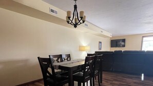 A dining area with a wooden table and chairs, a chandelier, a TV on the wall, and a window. - Our Boatyard Loft and Suites Unit A (Sandusky)