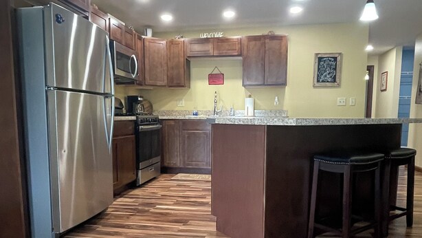 A modern kitchen with wooden flooring, stainless steel appliances, and pendant lighting. - Our Boatyard Loft and Suites Unit A (Sandusky)
