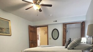 A bedroom with a bed, wooden flooring, a ceiling fan, a door, and a mirror. - Our Boatyard Loft and Suites Unit A (Sandusky)