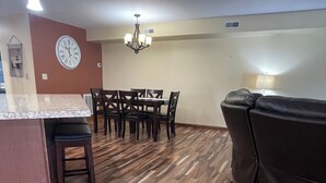 A modern living room with a brown leather sofa, a dining area with a wooden table and chairs, and a kitchen with a marble countertop and pendant lighting. - Our Boatyard Loft and Suites Unit A (Sandusky)