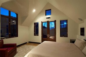 Un dormitorio con una cama grande, una silla roja y varias ventanas.