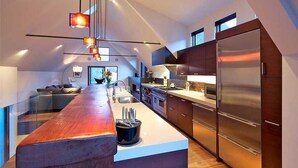 Une cuisine moderne dotée d’un grand îlot central, d’appareils électroménagers en acier inoxydable et d’une balustrade en verre donnant sur l’espace de vie.