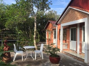 A residential building with a brick facade, a small porch, and a garden area with a statue, chairs, and a table. - Nam Thanh Homestay - Hostel (An Binh)