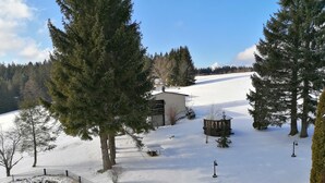 Schneebedeckte Landschaft mit einem eingezäunten Bereich, einem kleinen Gebäude und mehreren Bäumen.