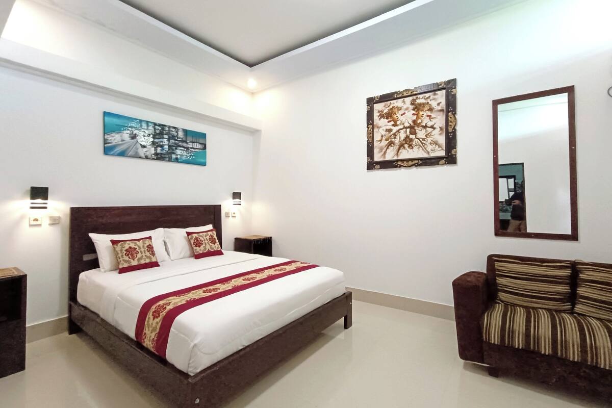 A bedroom with a large bed, a nightstand, a sofa, a painting, and a mirror.