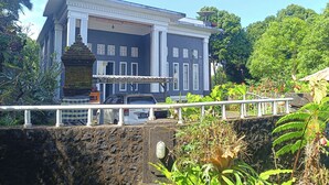 A large, two-story building with a dark facade and white trim, surrounded by lush greenery. - La Montana (Gobleg)
