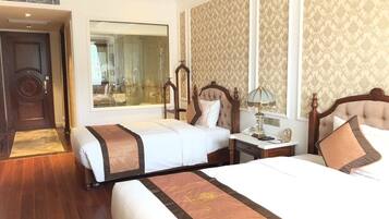 A hotel room with two beds, a large mirror, a desk with a lamp, and a view of the bathroom.