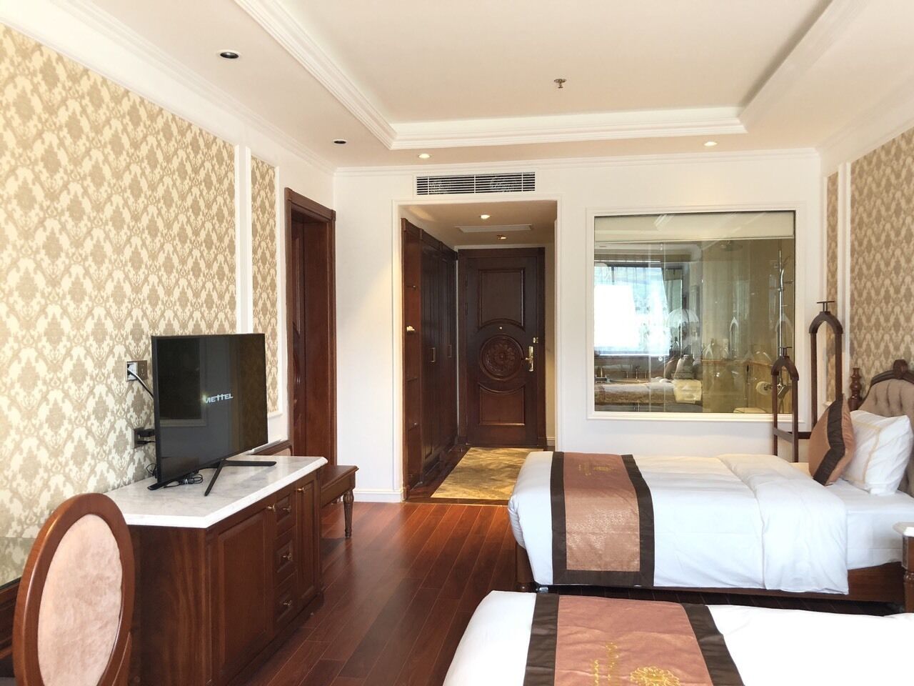 A hotel room with a bed, a desk with a television, a wardrobe, and a large window.