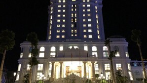 Un grand bâtiment illuminé, doté d’une entrée imposante, de colonnes et d’une enseigne indiquant « HÔTEL DE LUXE HOANG NAM ».