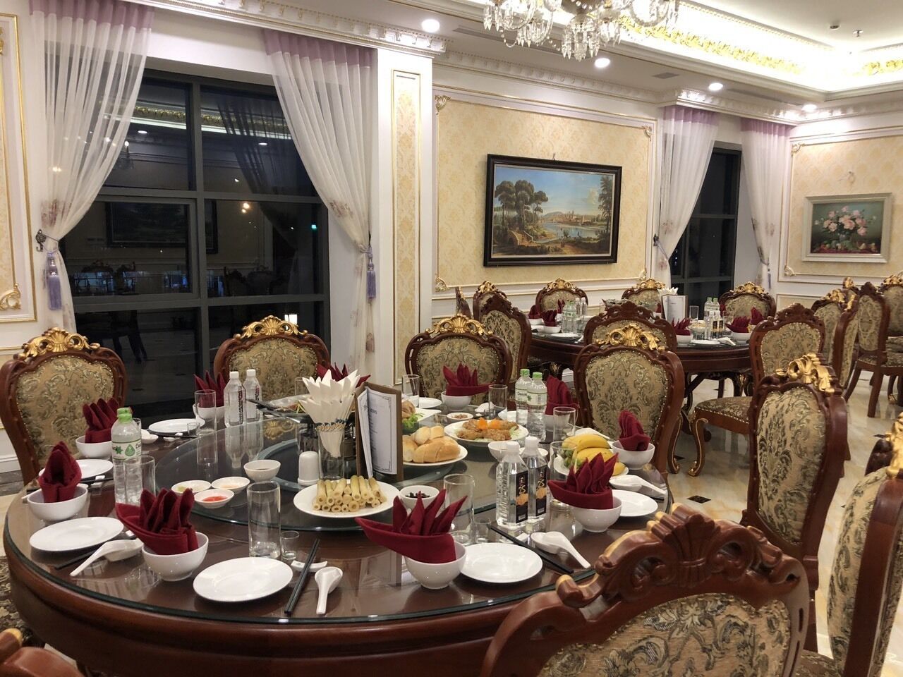 Une salle à manger élégante, avec des tables rondes, des chaises richement décorées et des lustres.