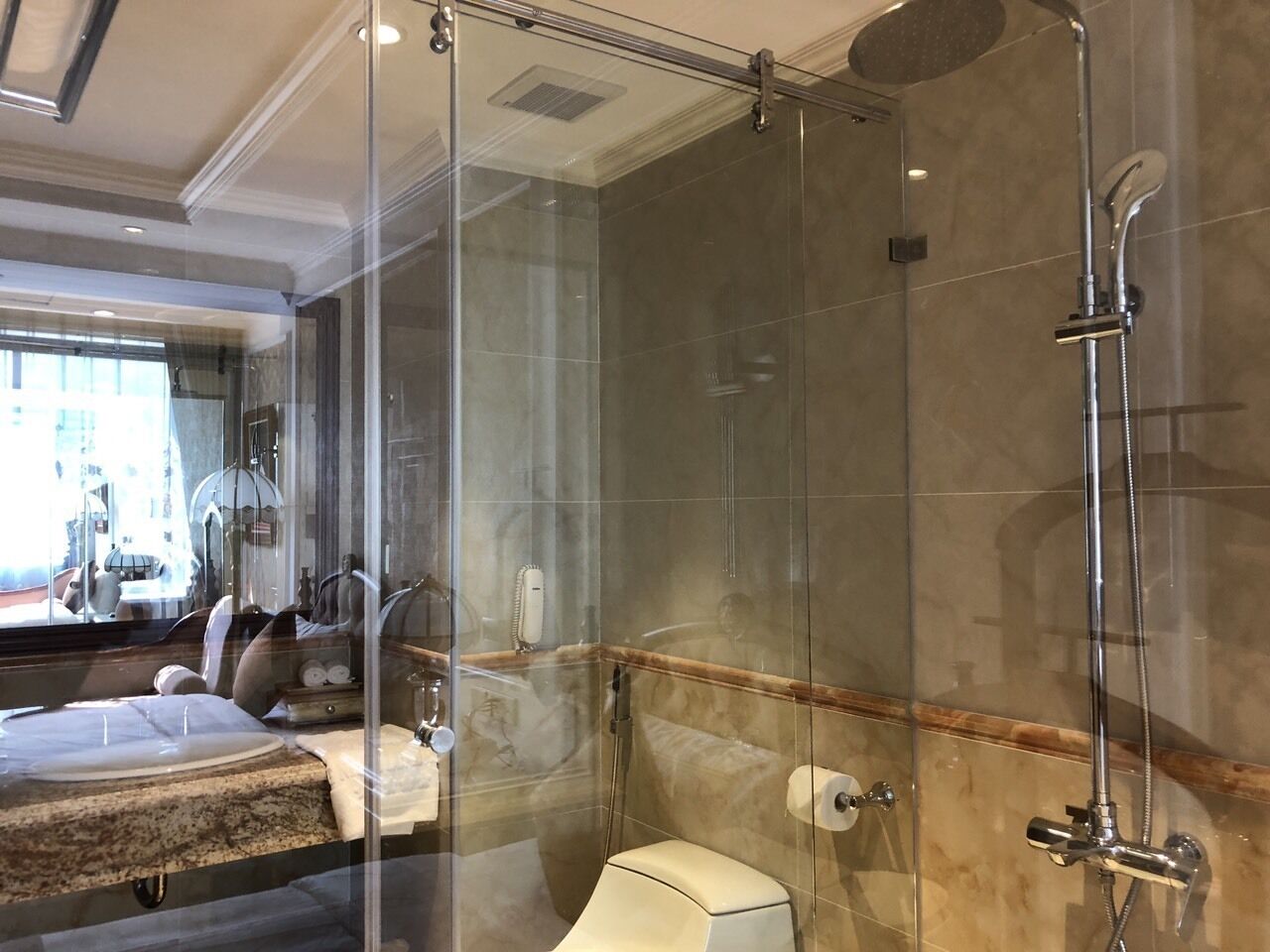 Un baño moderno con ducha envuelta en vidrio, pared con mosaicos de mármol y retrete a la vista.