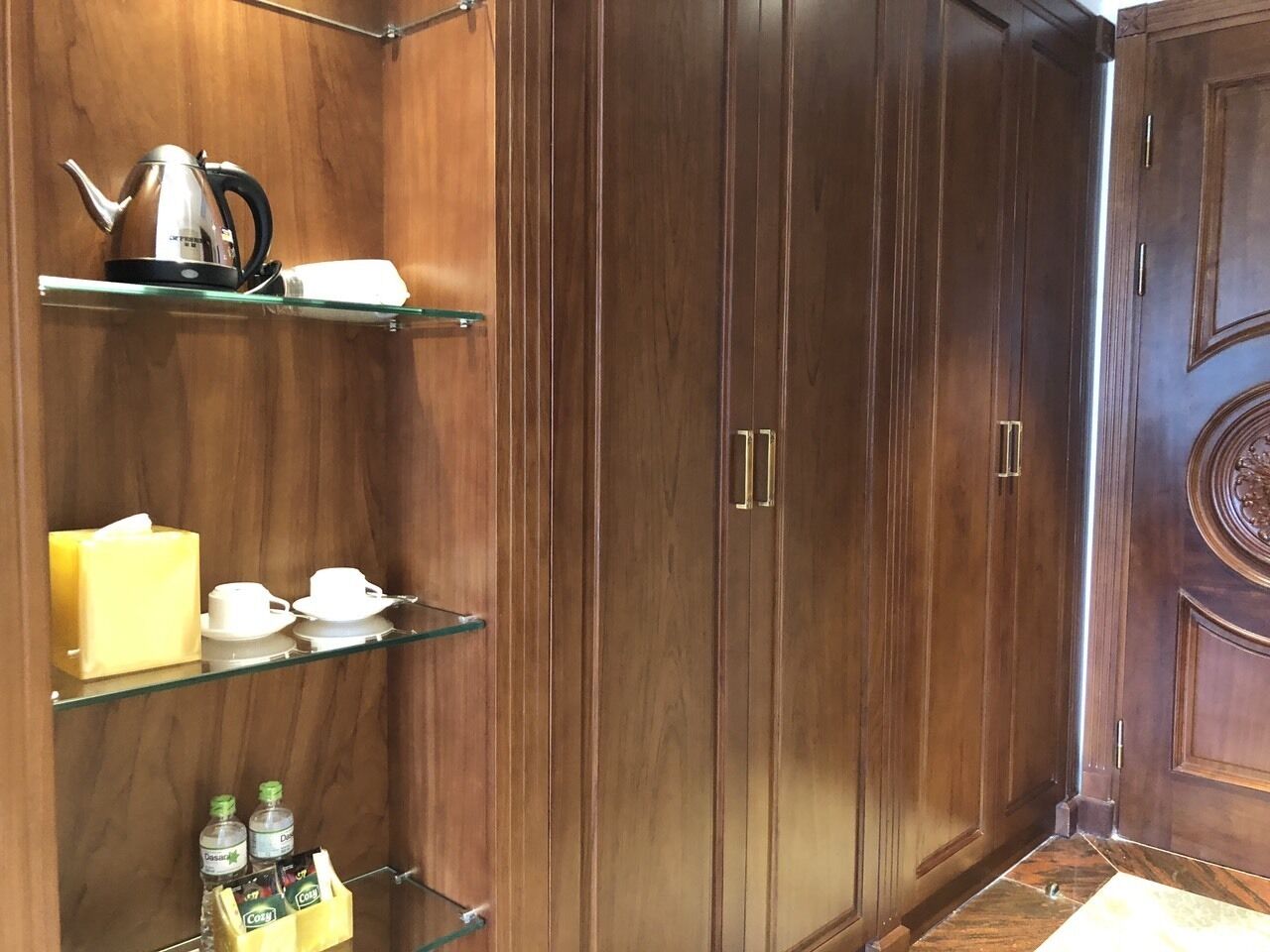 A wooden wardrobe with two doors, a shelf with a kettle, cups, and a tissue box.