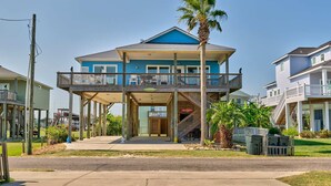 A two-story house with a balcony, a covered front porch, and a palm tree. - Bella Costa: Good Vibes & Ocean Tides (Bolivar Peninsula)