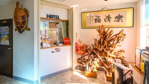 Zona de recepción de un hotel con una escultura de madera, un letrero que dice "HOTEL" y una obra de caligrafía enmarcada en la pared.