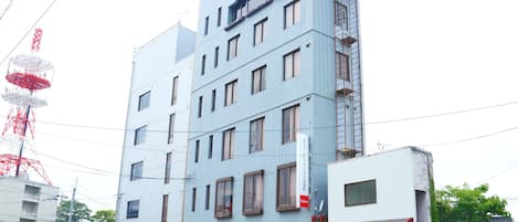 Un edificio de varios pisos con fachada azul, un letrero rojo en la parte superior y un toldo rojo en la planta baja.