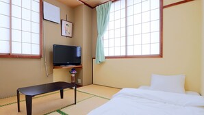 Una habitación con suelo de tatami, una cama, un televisor en una estantería y un cuadro en la pared.