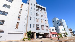 Un edificio de varios pisos con entrada de garaje, un letrero visible y un cielo azul despejado.