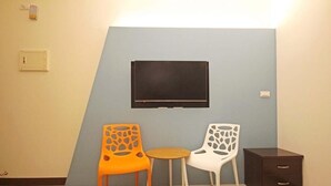 Una habitación con pared azul, un televisor de pantalla plana montado sobre una pequeña mesa redonda, y dos sillas con un diseño original y recortado.