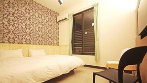 Un dormitorio con cama, una silla, una mesita pequeña, papel tapiz estampado y una ventana con cortinas.